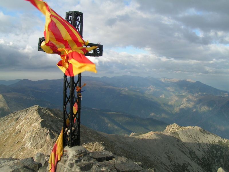 Croix sur sommet montagneux, drapeaux au vent.