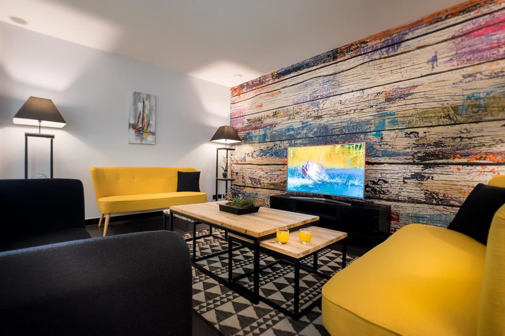 Salon moderne avec canapé jaune et télévision.